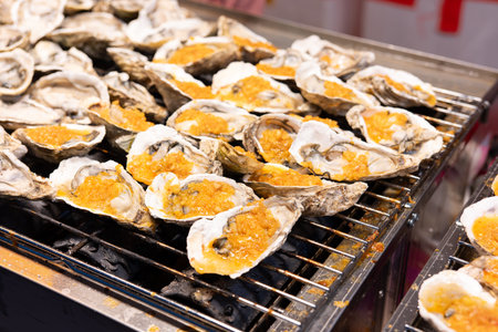 Grilled oysters with golden roe on metal grill at street food stallの写真素材
