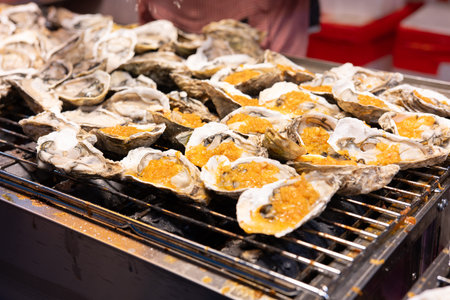 Grilled oysters on metal grill with golden roe, street food scene at nightの写真素材