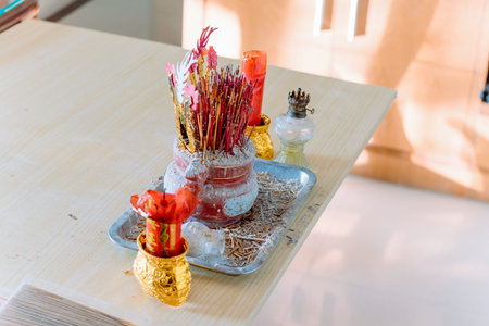 Incense sticks burning in ceremonial bowl on wooden table with red candles and ritual offeringsの写真素材