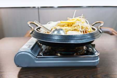 Hot pot with noodles and vegetables cooking on portable stove at dining table