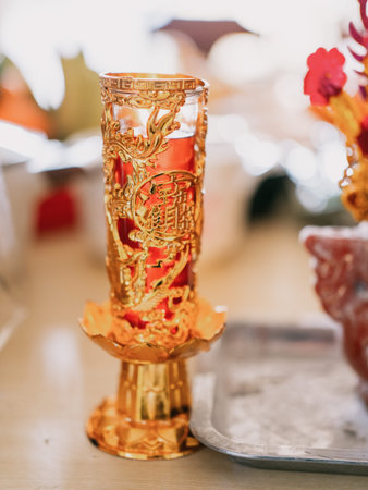 Golden ornate candle holder with red wax and traditional Chinese characters, placed on table during...
