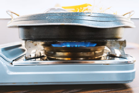 Gas stove with blue flame heating pan containing food on portable burnerの写真素材