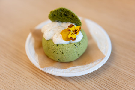 Matcha green tea dessert with whipped cream and edible flower on white plate