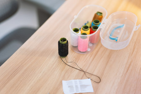 Sewing threads in plastic case on wooden table with needle and instruction paper