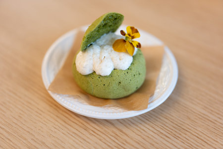 Green matcha dessert with whipped cream and edible flower on white plate