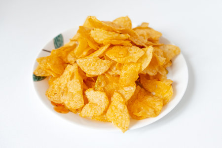 Crispy golden potato chips piled on white plate with green leaf design, isolated on white backgroundの写真素材