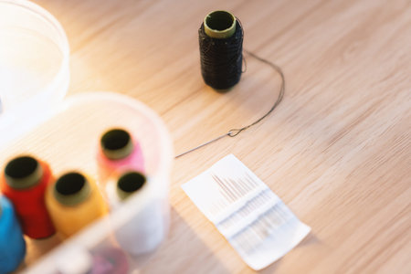 Sewing needle and thread spools on wooden table with sewing tools and fabric supplies