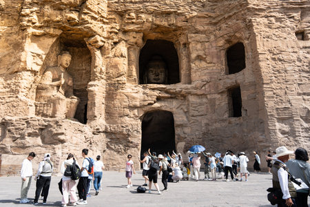 Tourists Explore Ancient Rock-Carved Buddha Statues in Historic Cave Temple Complexの写真素材