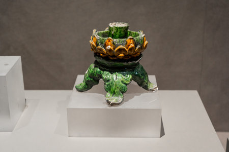 Ancient ceramic incense burner with green glaze and orange floral motifs displayed on white pedestalの写真素材