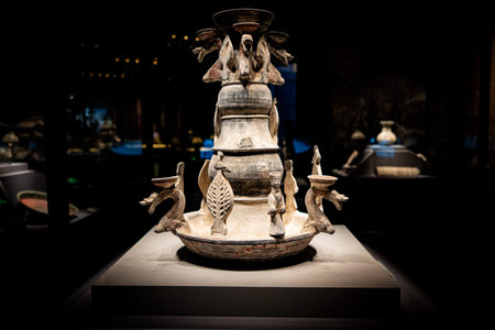 Ancient ceramic vessel with bird and dragon motifs displayed in museum under spotlightの写真素材