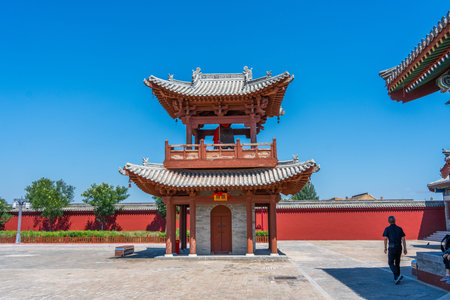 Traditional Chinese temple gate with red walls under clear blue sky, person walking nearby