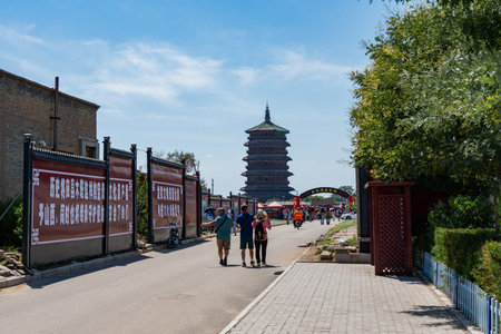 Tourists walking toward ancient pagoda under clear blue sky with trees and banners along pathway