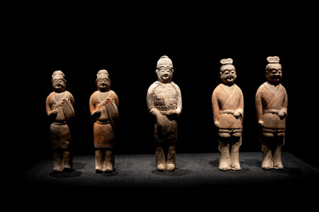 Ancient Chinese terracotta figurines displayed in museum with dark backgroundの写真素材