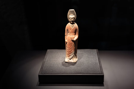 Ancient Chinese terracotta figurine displayed in museum exhibit under spotlight
