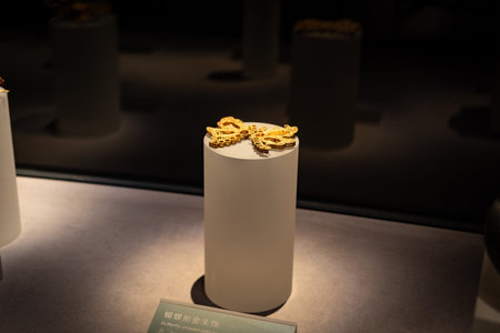 Golden ornamental artifact displayed on white pedestal in museum exhibit under focused lighting