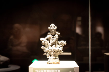 Ancient bronze statue of deity displayed in museum glass case with dim lighting and reflective...