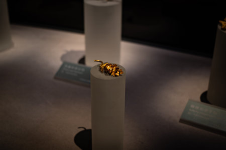 Golden Insect Artifact Displayed on White Cylinder in Museum Exhibit