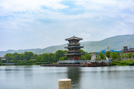 Traditional Chinese pagoda on lake island with mountain backdrop under cloudy sky