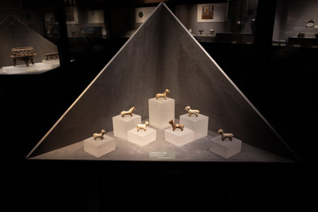 Ancient golden animal figurines displayed in museum glass pyramid case with white pedestals and dark...
