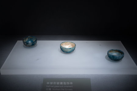 Ancient blue-glazed ceramic bowls displayed in museum exhibit with white pedestal and dark...