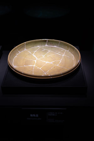 Ancient ceramic plate with crackle glaze displayed in museum under spotlightの写真素材