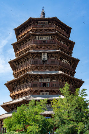 Ancient Wooden Pagoda with Multiple Eaves Under Blue Sky, Surrounded by Green Trees