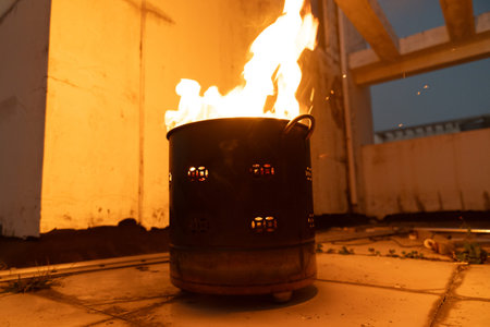 Burning fire in metal barrel on rooftop at dusk with warm glow and sparks flying