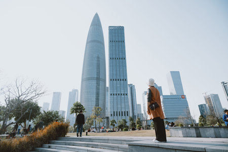 Modern urban skyline with tall glass skyscrapers, people walking on steps in foreground under clear skyの写真素材