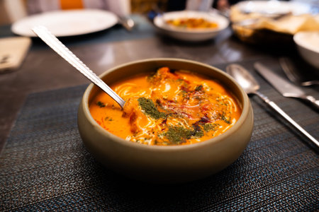 Indian Curry Soup in Clay Bowl with Spoon on Dark Tablecloth, Restaurant Setting