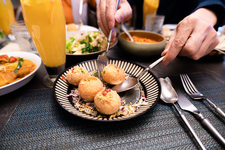 Hands serving Indian Pani Puri on patterned plate with chutney and drinks at dining table