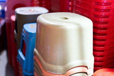 Stacked plastic stools in vibrant colors at a market stall, featuring red blue and beige seats with...