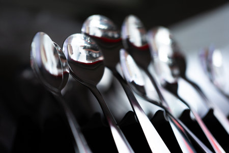 Shiny metal spoons arranged in row with reflective surfaces and dark background