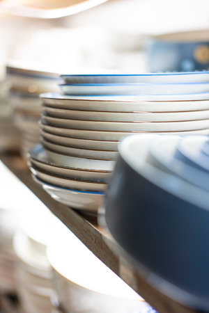 Stacked ceramic plates with blue rims displayed on wooden shelf in softly lit kitchen setting