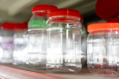 Clear plastic jars with red lids lined on shelf in store or pantry, empty and ready for use