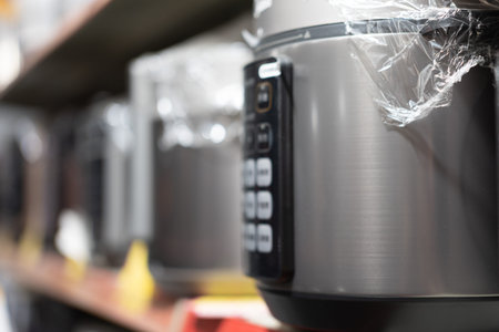 Stainless steel rice cooker on store shelf with plastic wrap, blurred background of kitchen...