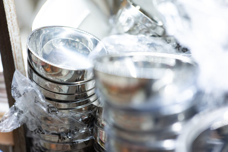 Stacked stainless steel bowls wrapped in plastic, commercial kitchenware display, reflective...