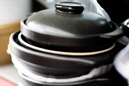 Black ceramic pot with lid stacked on kitchen counter, traditional Asian cooking vessel, dark glossy...