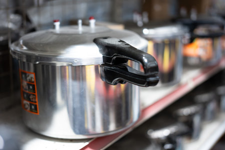Stainless steel pressure cooker on retail shelf with black handle and safety valve, commercial...