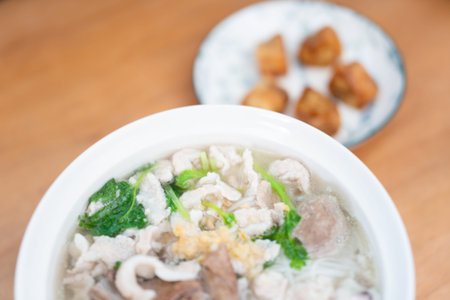 Cantonese-style pork rib soup with greens and fried tofu cubes served in white bowl on wooden table