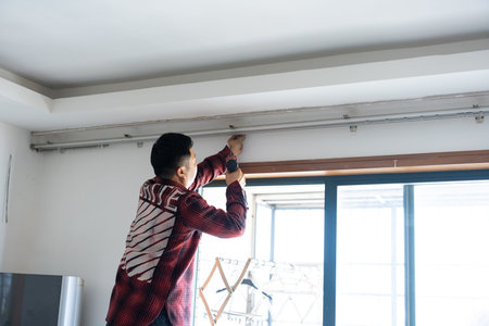 Man installing window blind track in modern apartment room with large glass window, urban home