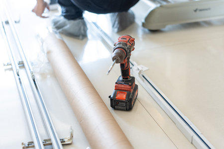 Red cordless drill resting on floor near metal frames and cardboard roll during installation inの写真素材