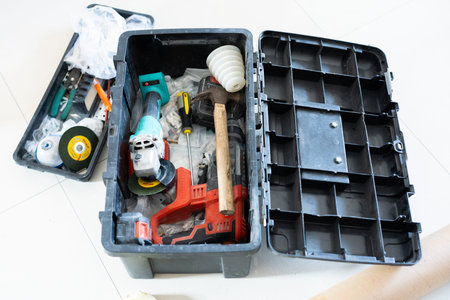 Open black toolbox with power tools and hardware items on white floor