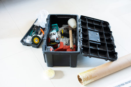 Open black toolbox with power tools and hardware on white floor, construction or DIY project setup