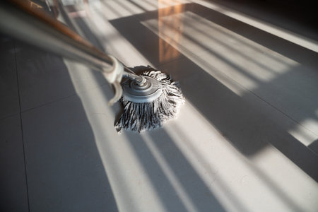 Wet mop cleaning tiled floor with sunlight shadows in modern home interior
