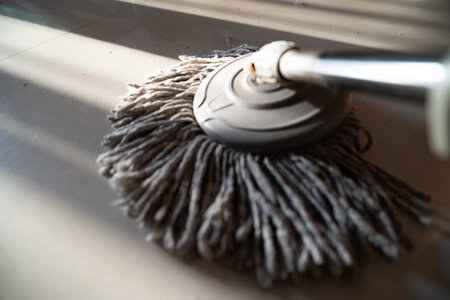 Wet mop with fibrous head cleaning tiled floor in indoor setting