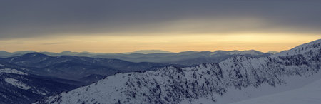 Winter mountain landscape with cloudy sky, lit by the sunset. Panoramic photo.