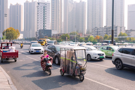 People on electric bicycle with colourful windshield on crossroad, Hefei, China.のeditorial素材