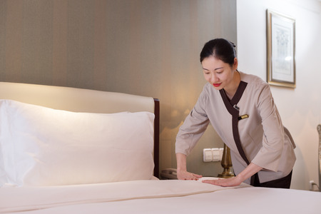 young chinese woman housekeeper makes bed in modern hotelのeditorial素材