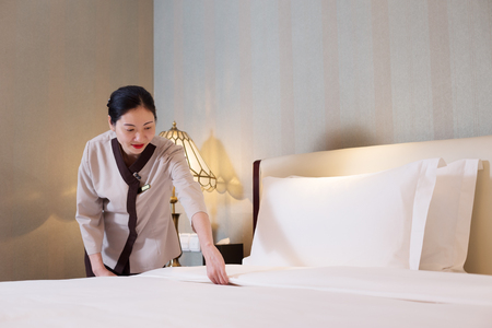 young chinese woman housekeeper makes bed in modern hotelのeditorial素材
