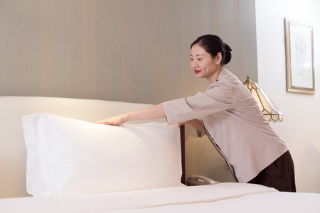 young chinese woman housekeeper makes bed in modern hotelのeditorial素材